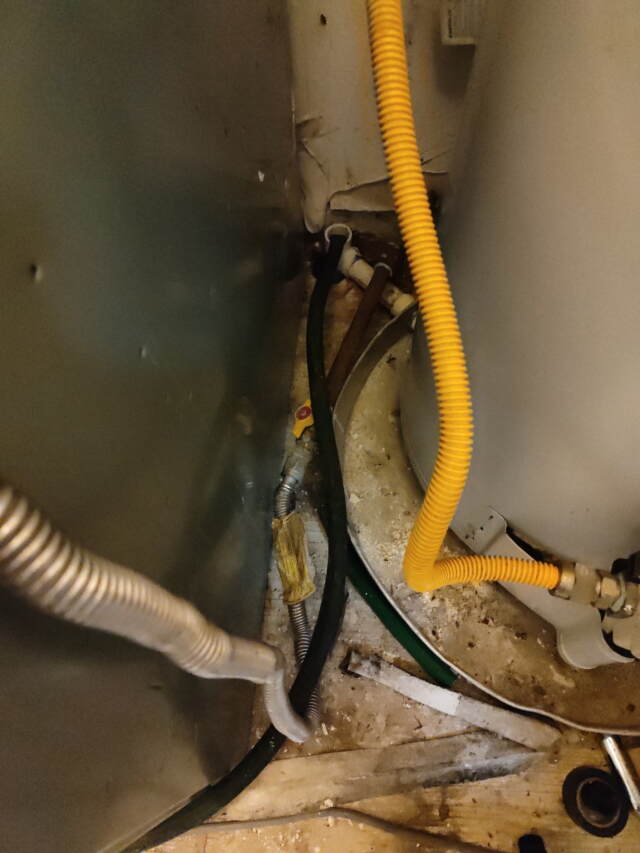 This is looking between narrow gap of the gas heater and water heater where the opening of the drain is that was clogged up.
