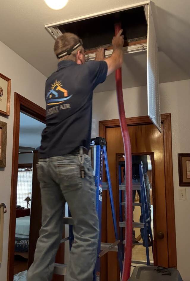 The technician cleaning inside the duct using red vacuum hose with a brush attached to the end.